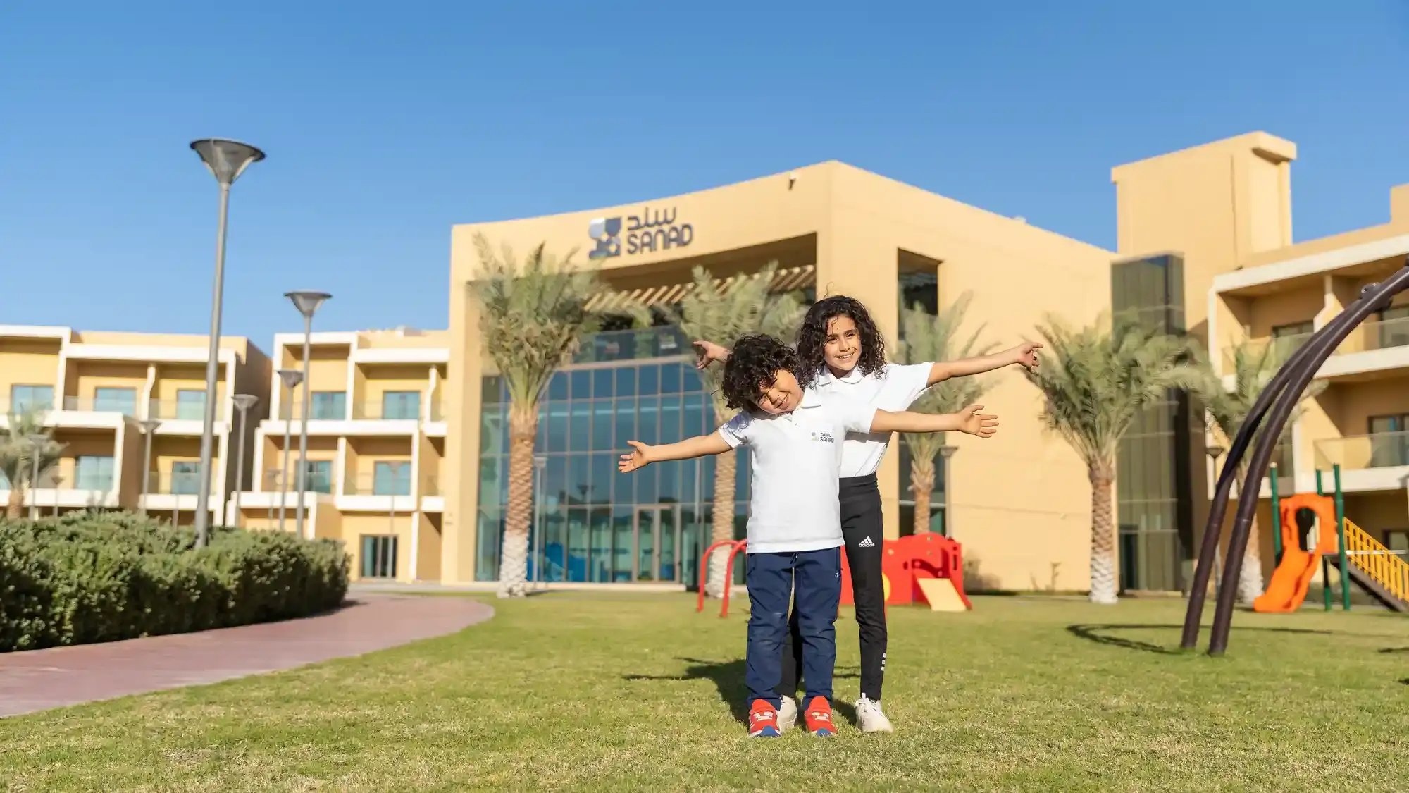 Children enjoying inclusive outdoor play in front of the Sanad Village campus and accessible playground in Dubai